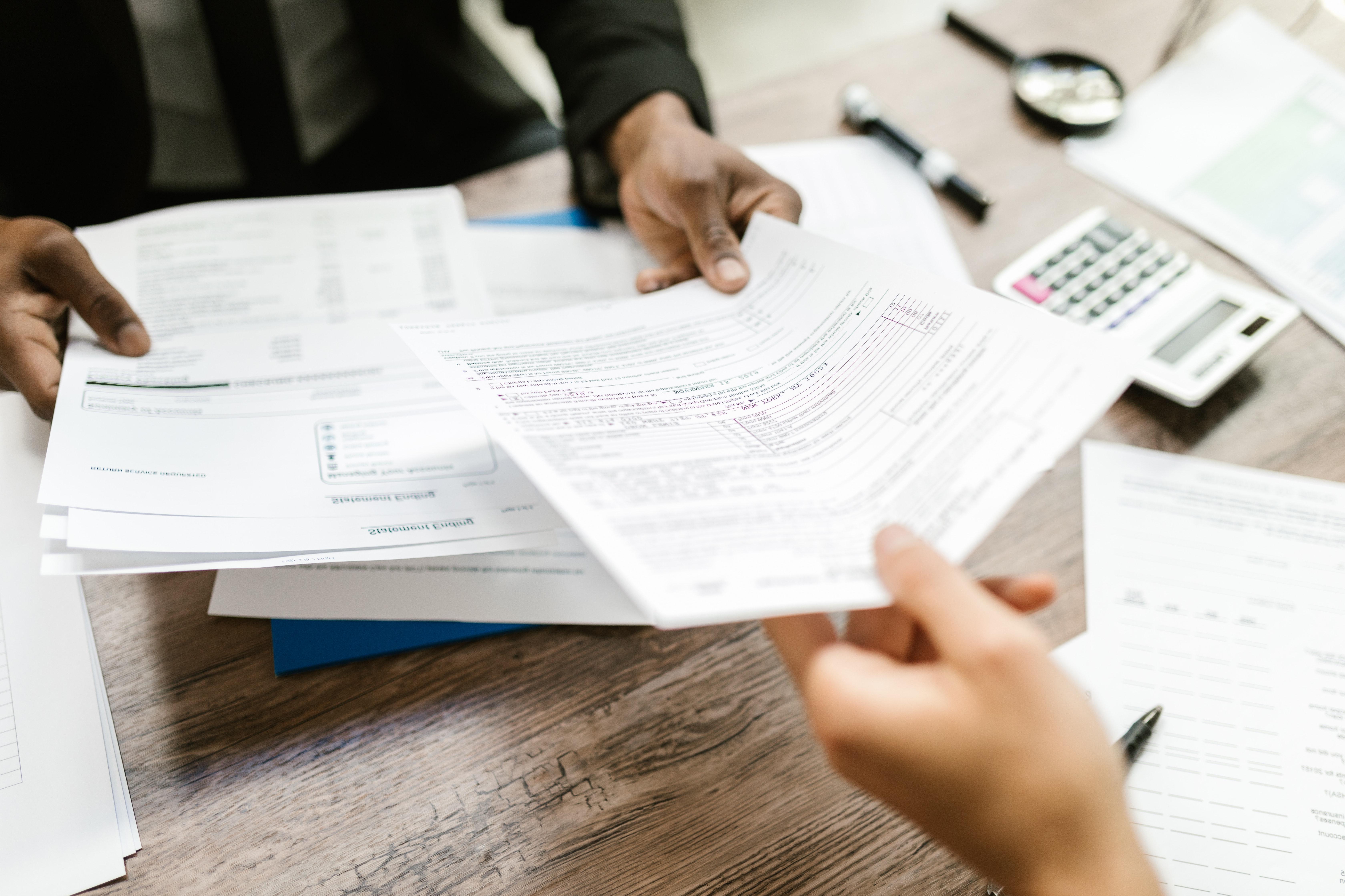 Two people sitting across from each other at a desk passing documents